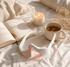 Masseur oculaire LED Satilune posé sur un lit avec une tasse de thé et une bougie, routine bien-être