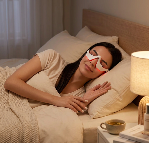 Femme détendue au lit portant le masseur oculaire LED Satilune à lumière rouge